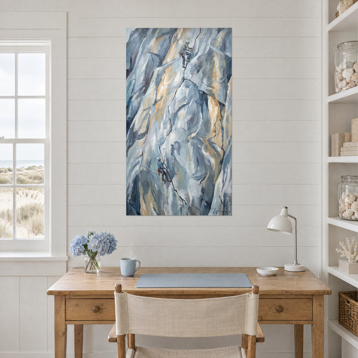 Quadro parete rocciosa a pittura materica, crepa nera, due minuscoli alpinisti, toni grigio-azzurri e ocra, sopra una scrivania in legno chiaro