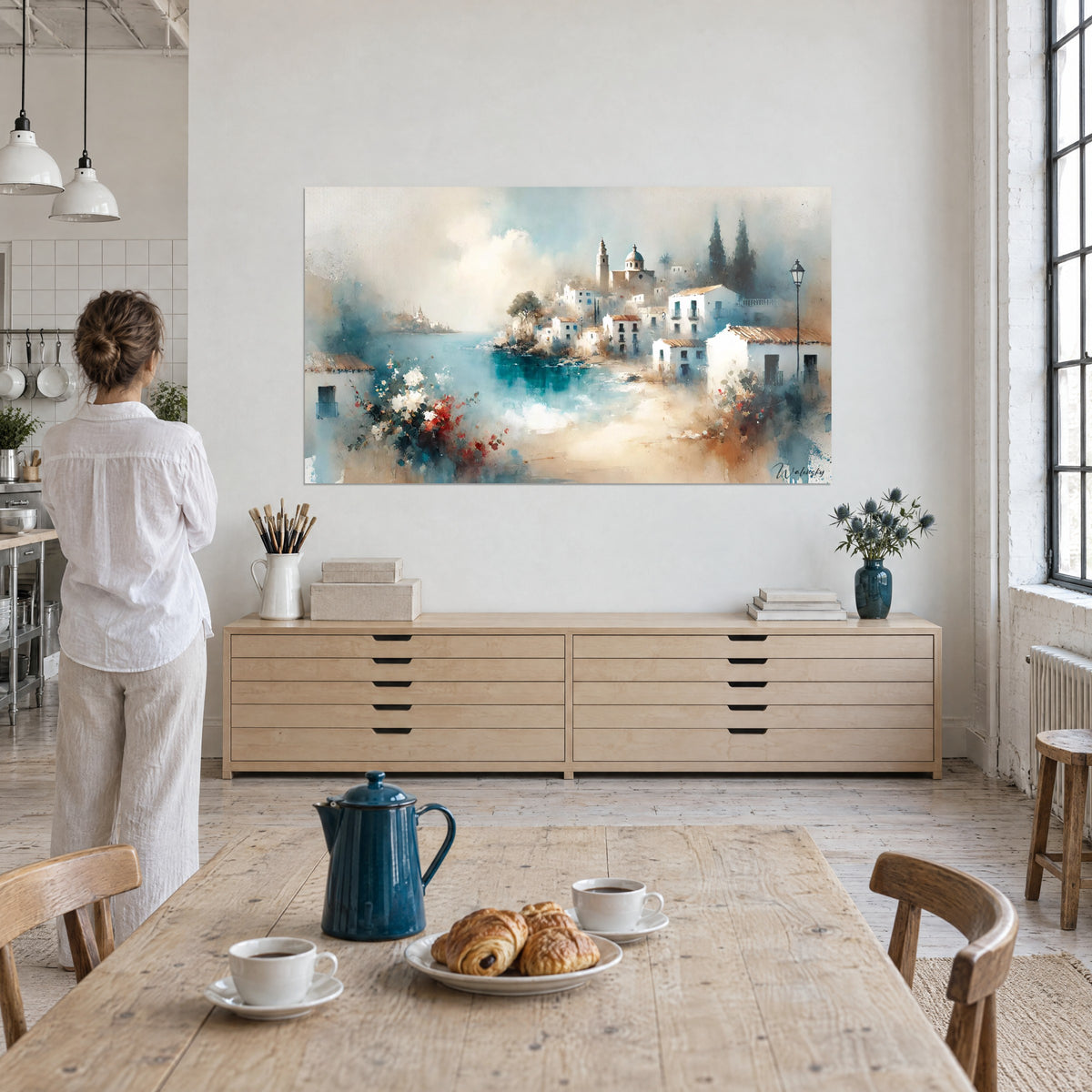 Tableau petit port espagnol en lavis bleu pétrole et sable, une femme en chemise blanche de dos devant lui, buffet en bois clair et café