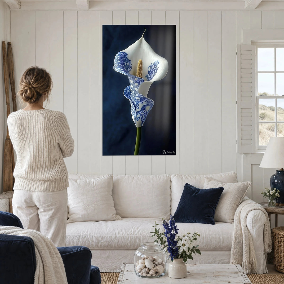 Wall art white arum with cobalt blue patterns on navy background, woman seen from behind, above a sofa in a bright living room