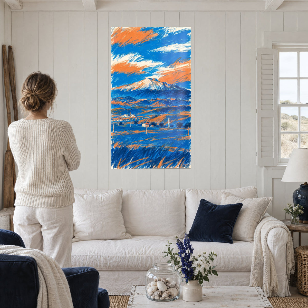 Tableau Etna enneigé sous nuages orange et bleu, traits de crayon croisés, au-dessus d'un canapé dans un salon lumineux