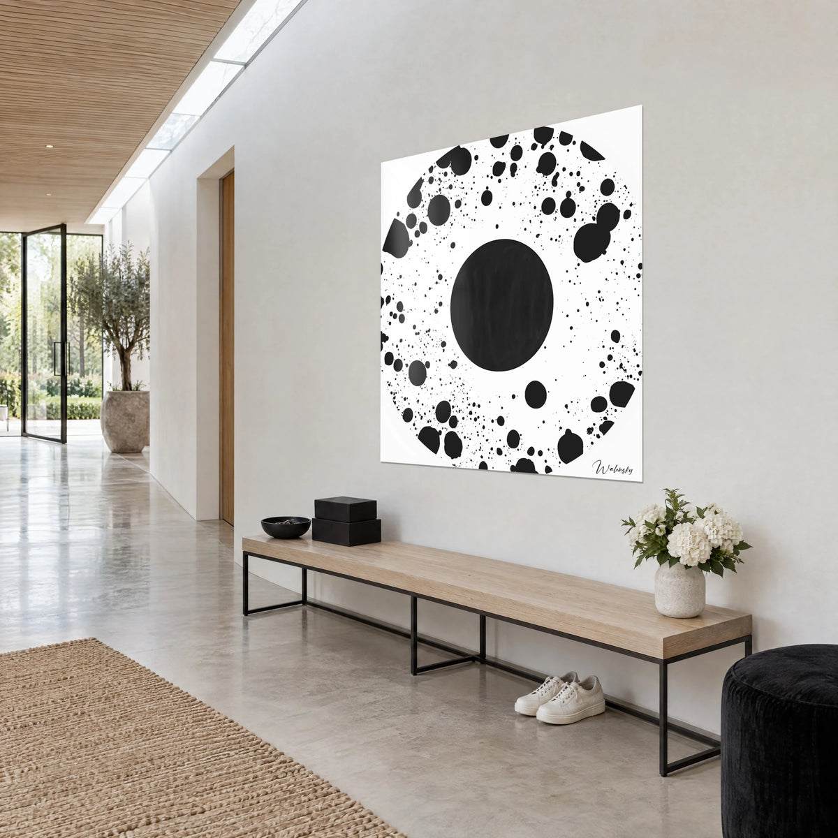 Tableau astre noir mat entouré de gouttes et de taches d'encre éparses sur blanc pur, vu en trois-quarts dans un couloir clair, bois et béton