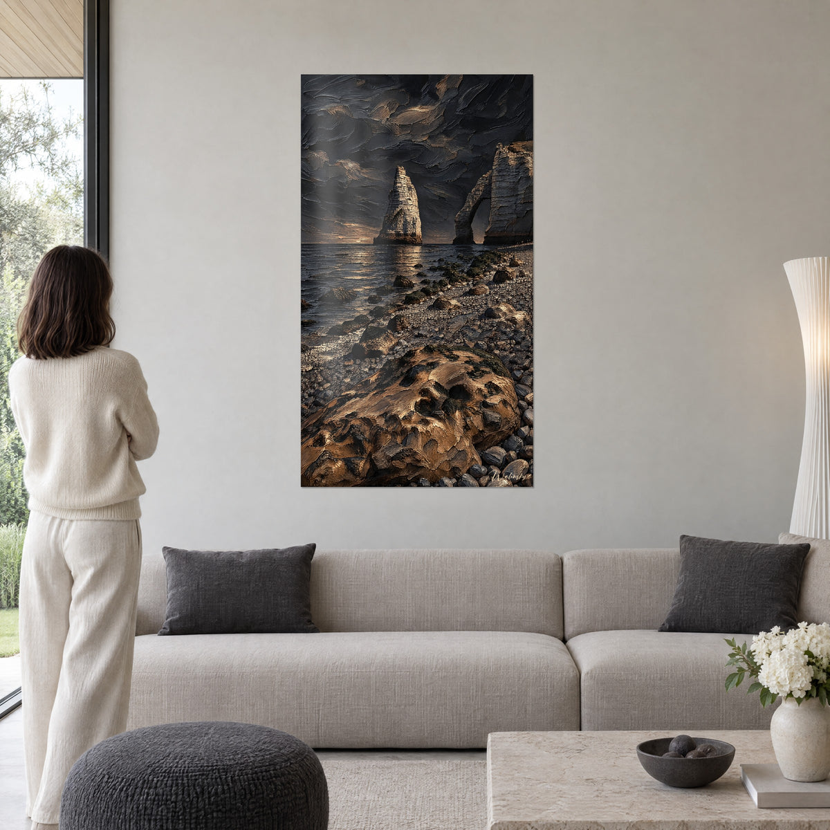 Tableau falaise d'Étretat anthracite et dorée, aiguille de craie sous un ciel orageux, femme de dos, au-dessus d'un canapé dans un salon lumineux