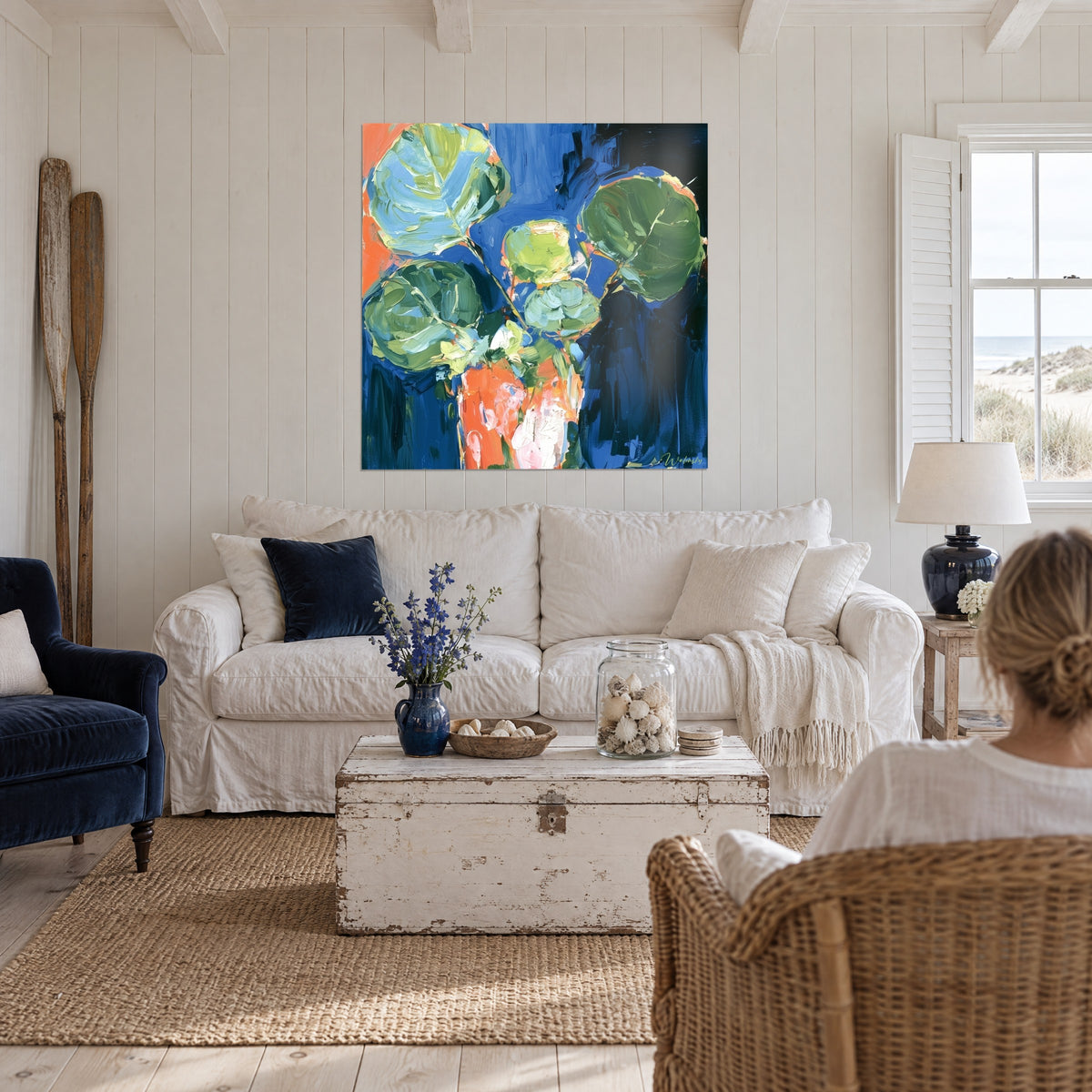Schilderij eucalyptus met ronde salieblauwgroene en kobaltblauwe bladeren, oranje vaas, boven een bank in een lichte woonkamer