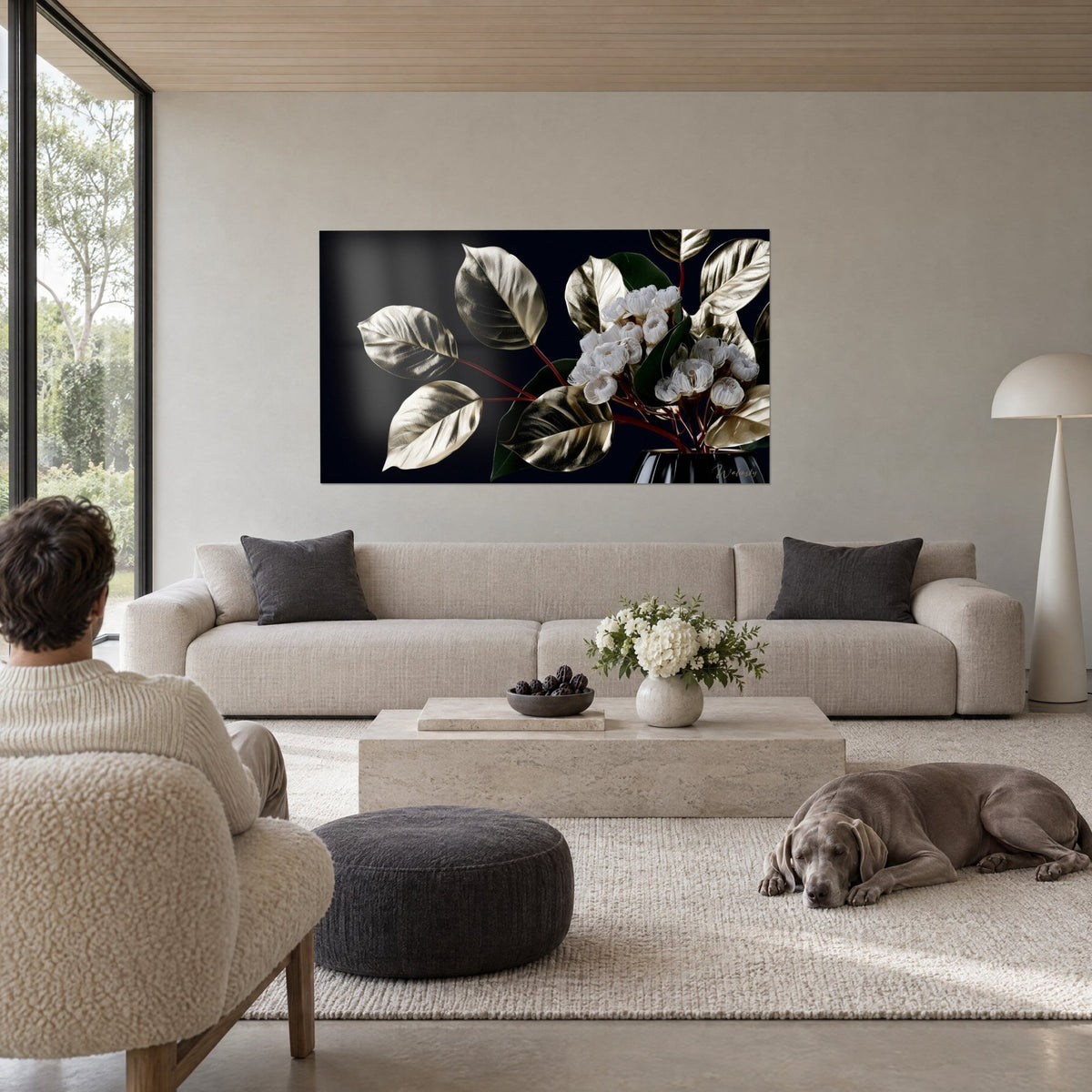 Schilderij van eucalyptus met gouden bladeren en witte bloemen op zwarte achtergrond, man van achteren en hond, boven een bank in een lichte woonkamer