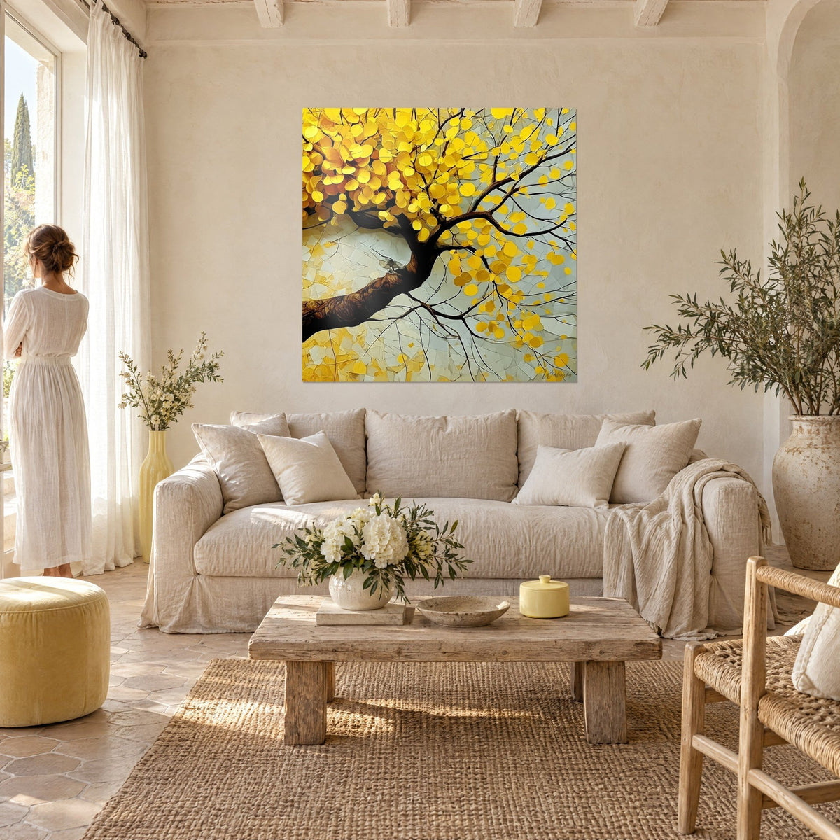 Wall art tree with round saffron-yellow leaves on brown branches, pearl grey background, woman seen from behind, above a sofa in a bright living room