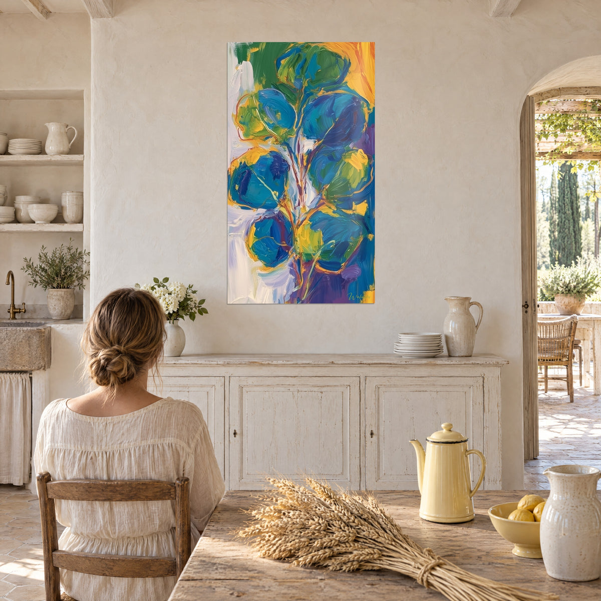 Tableau bouquet d'eucalyptus aux pétales ronds indigo et verts, touches jaunes, face à une femme attablée dans une cuisine de mas
