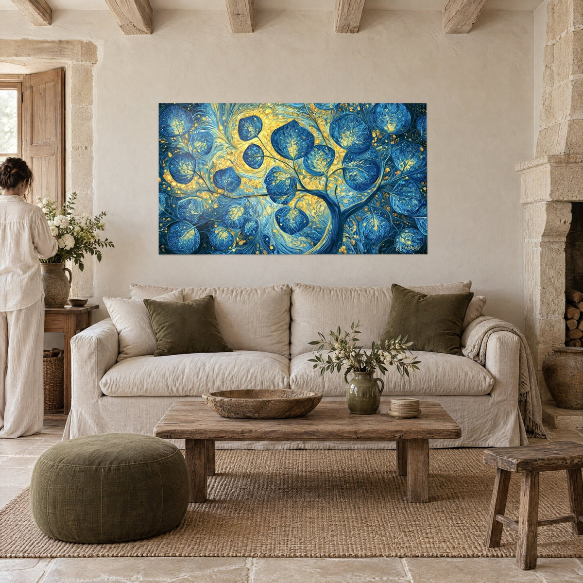 Wall art tree with large navy blue leaves on a golden yellow background, woman seen from behind, above a sofa in a bright living room