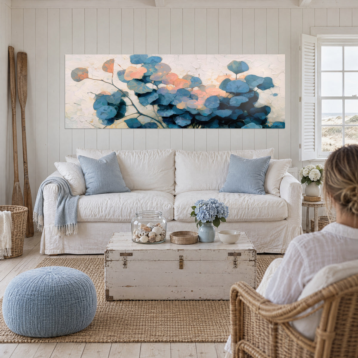 Tableau feuilles d'eucalyptus bleu acier et corail sur fond crème craquelé, au-dessus d'un canapé dans un salon lumineux