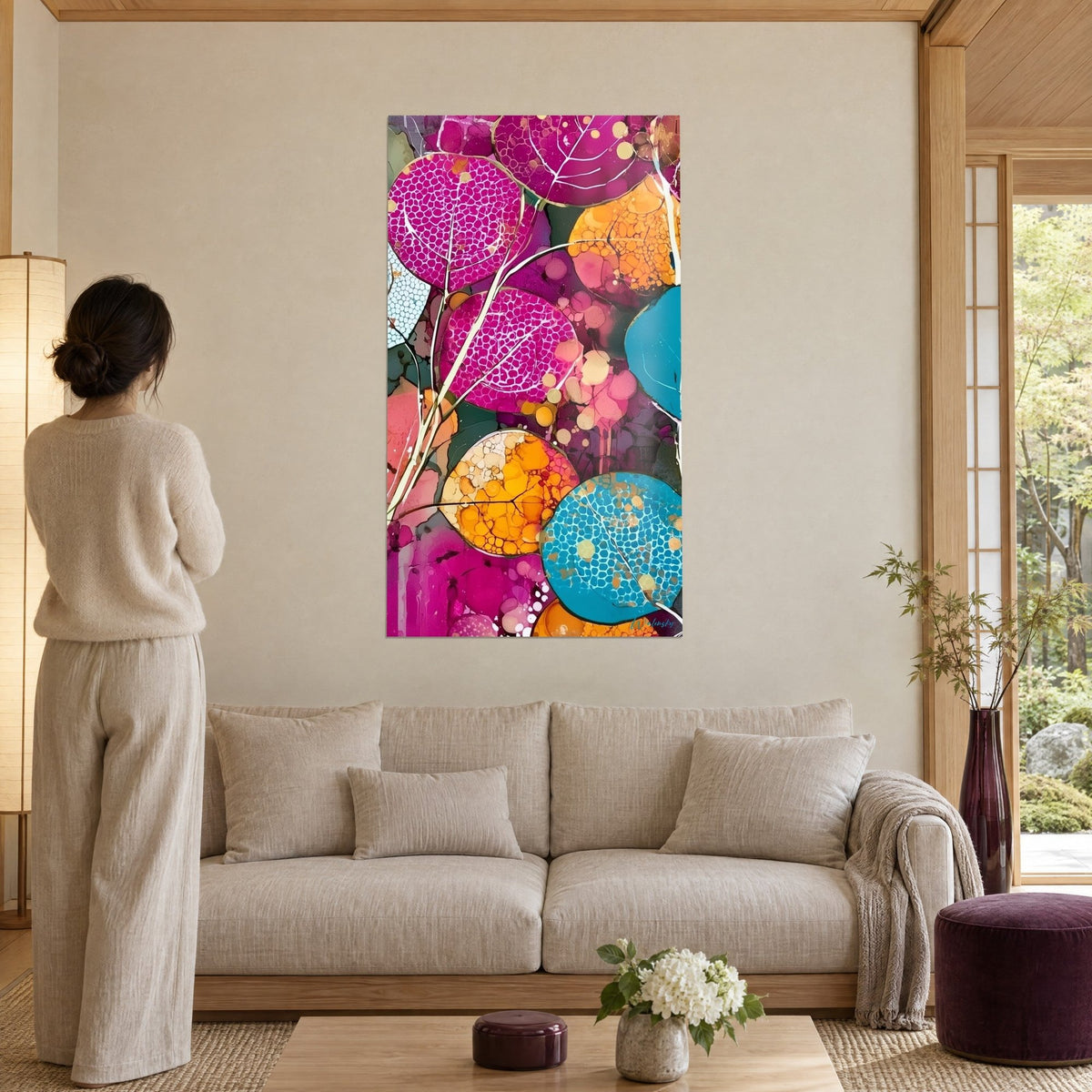 Schilderij met ronde fuchsia en oranje bladeren, lichte nerven en gouden sap, vrouw van achteren, boven een bank in een lichte woonkamer
