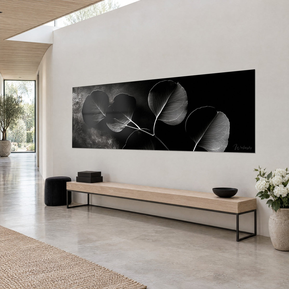 Wall art panoramic eucalyptus branch, anthracite and pearl grey leaves on deep black background, white wall and light wood bench