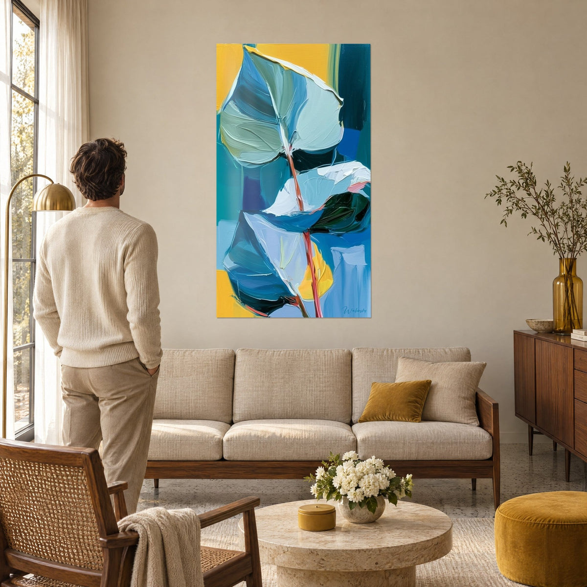 Wall art glacier blue eucalyptus leaves with coral stems on a mustard yellow background, a man seen from behind above a sofa in a bright living room
