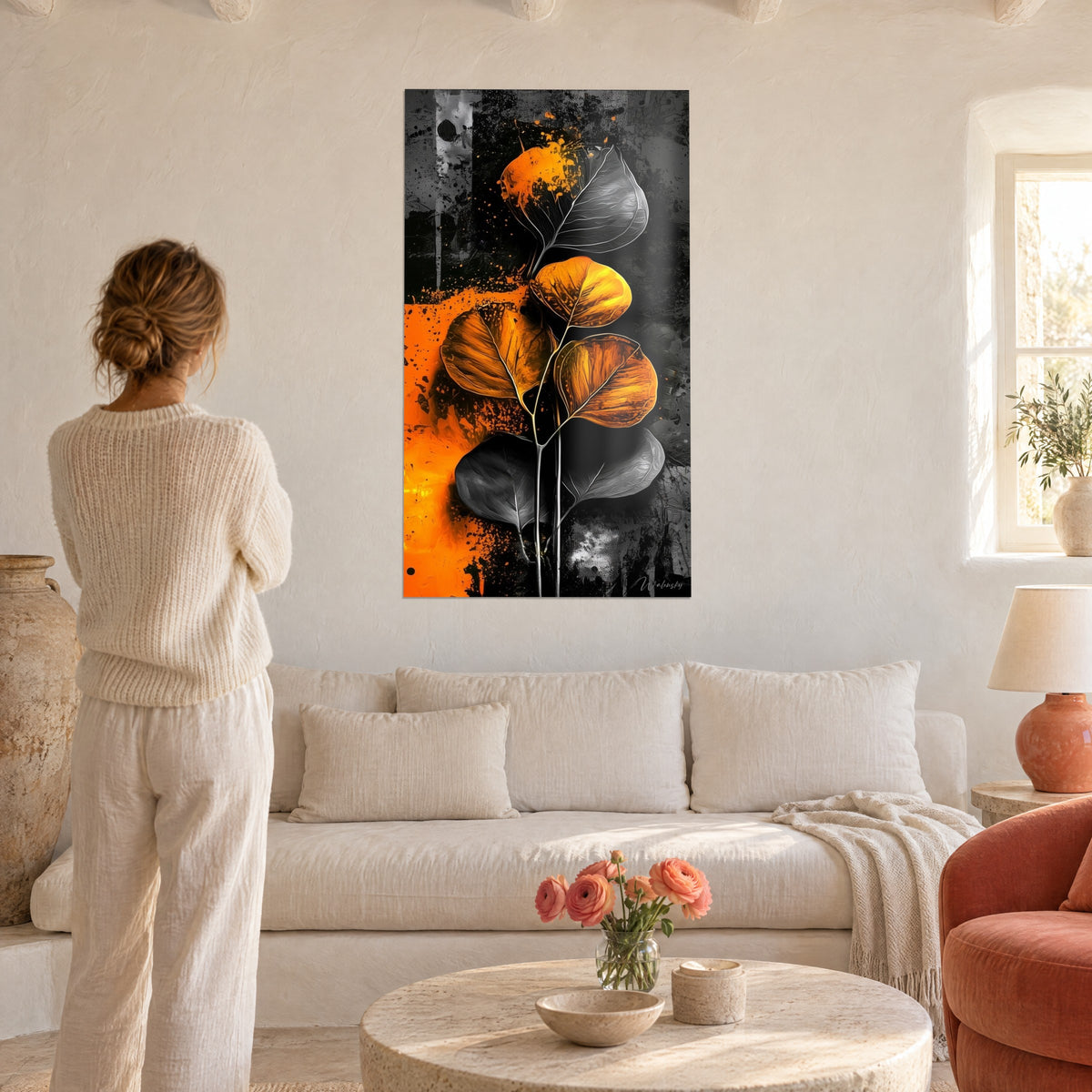 Tableau feuilles d'eucalyptus rondes orange et grises, nervures argentées, femme de dos, au-dessus d'un canapé dans un salon lumineux
