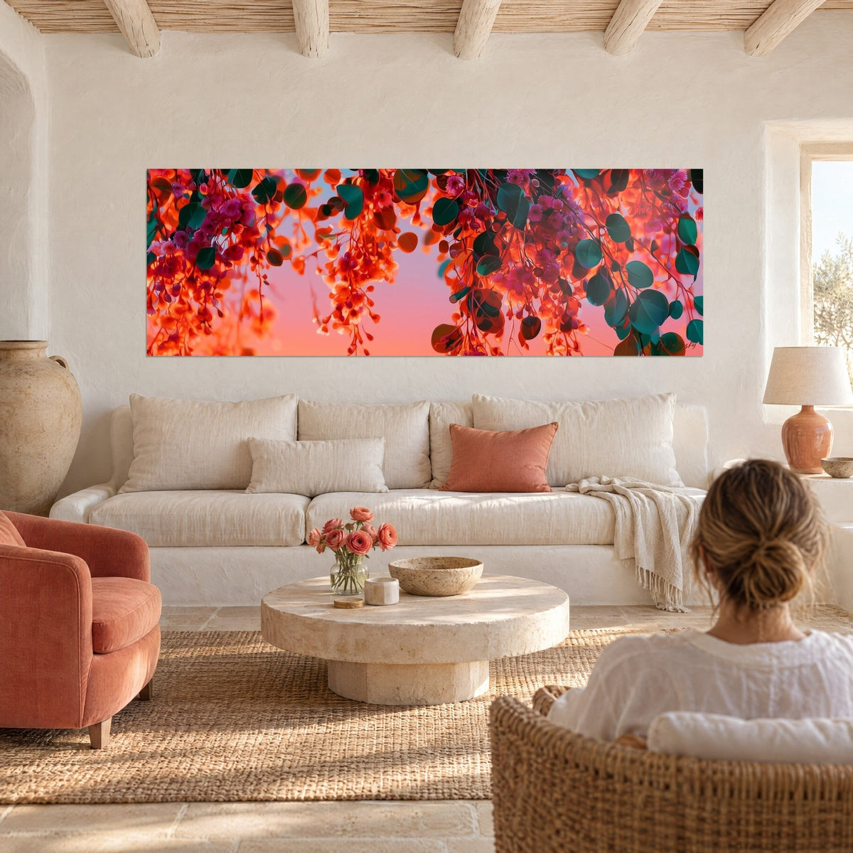 Gemälde mit orangefarbenen Eukalyptustrauben und tannengrünen Blättern vor rosa Himmel, Frau von hinten, über einem Sofa in einem hellen Wohnzimmer