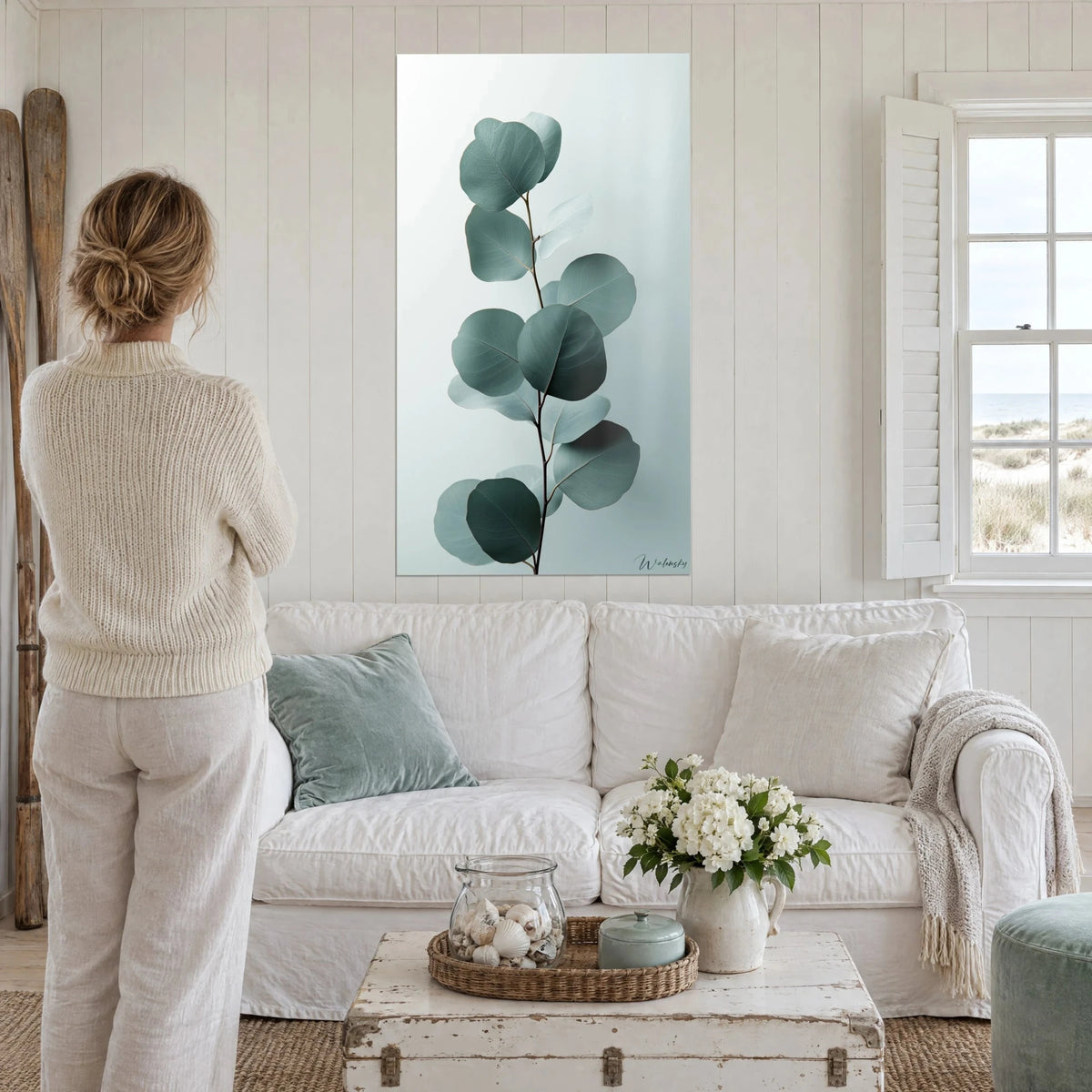 Wall art eucalyptus branch with round verdigris leaves on a pearl grey background, above a sofa in a bright living room