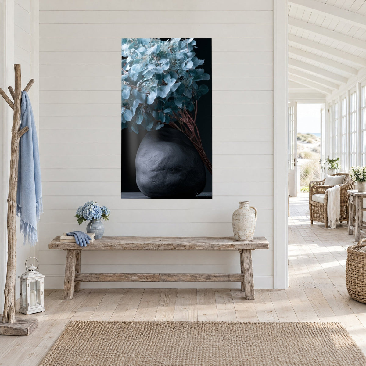 Schilderij antraciet stenen vaas met zilverkleurige eucalyptusbladeren, gekruiste roestkleurige stelen, tegen een witte houten lambrisering aan zee