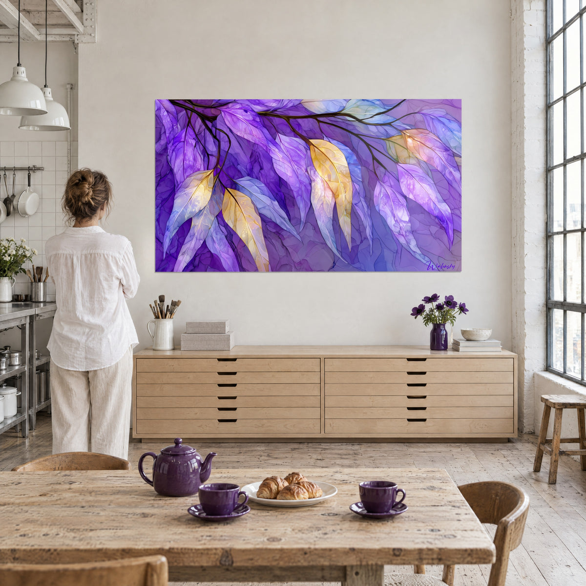 Tableau rameau aux grandes feuilles diaphanes bleu-violet et or, regardé par une femme de dos, dans un loft baigné de lumière