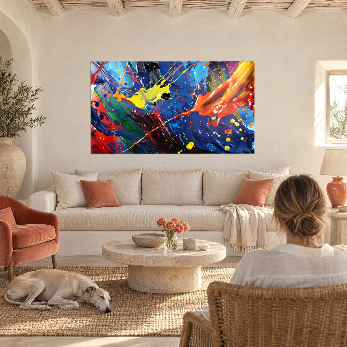 Tableau éclaboussures de peinture jaune et orange sur fond bleu cobalt, vu par une femme de dos, au-dessus d'un canapé dans un salon lumineux
