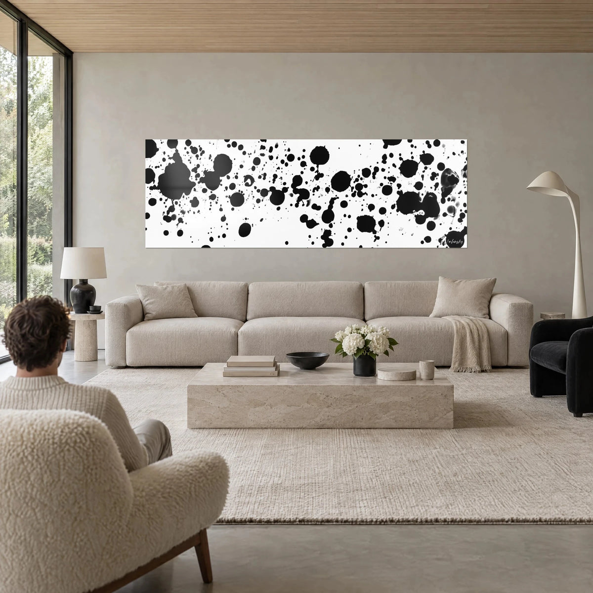 Quadro con schizzi di inchiostro nero su fondo bianco, macchie grandi e gocce sottili, sopra un divano in un soggiorno luminoso