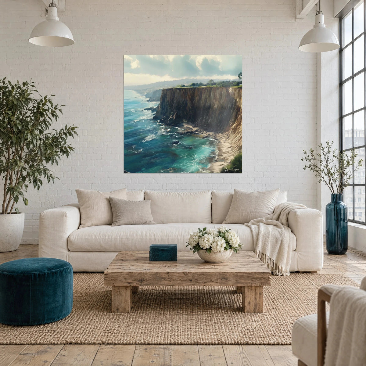 Wall art of a brown cliff overlooking turquoise sea, white foam and cloudy sky, above a sofa in a bright living room