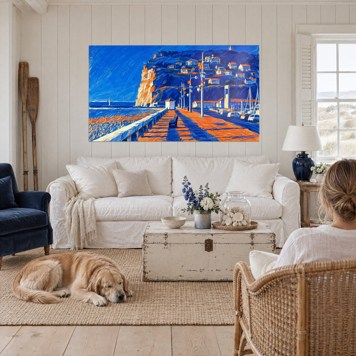 Schilderij oranje klif van Kaap Fagnet boven een blauw-koraalkleurige pier, liggende retriever, boven een bank in een lichte woonkamer