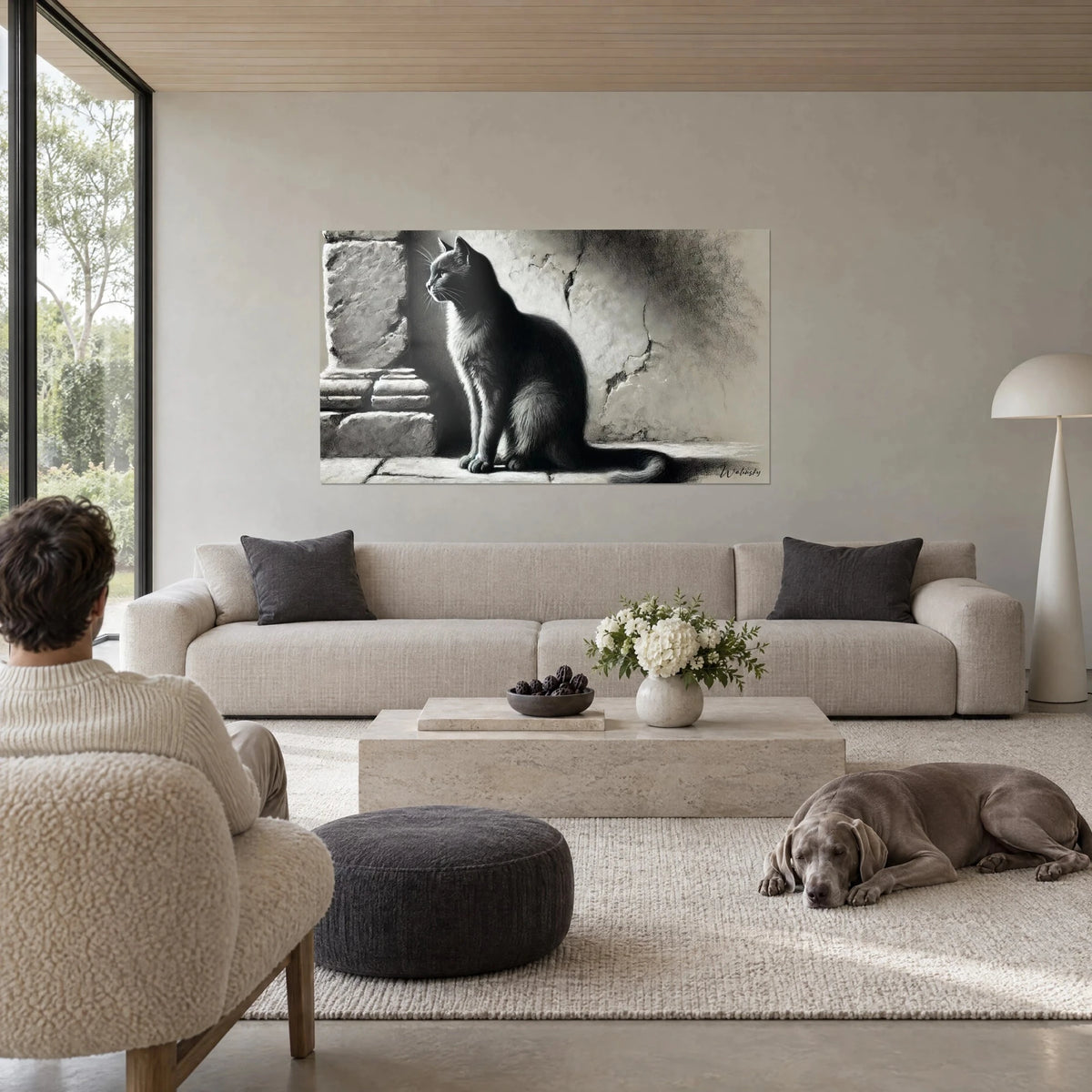 Gemälde Sitzende Katze im Profil, schwarz-graue Kohlezeichnung, Rücken zweier Personen und ein Weimaraner, über einem Sofa in einem lichtdurchfluteten Wohnzimmer