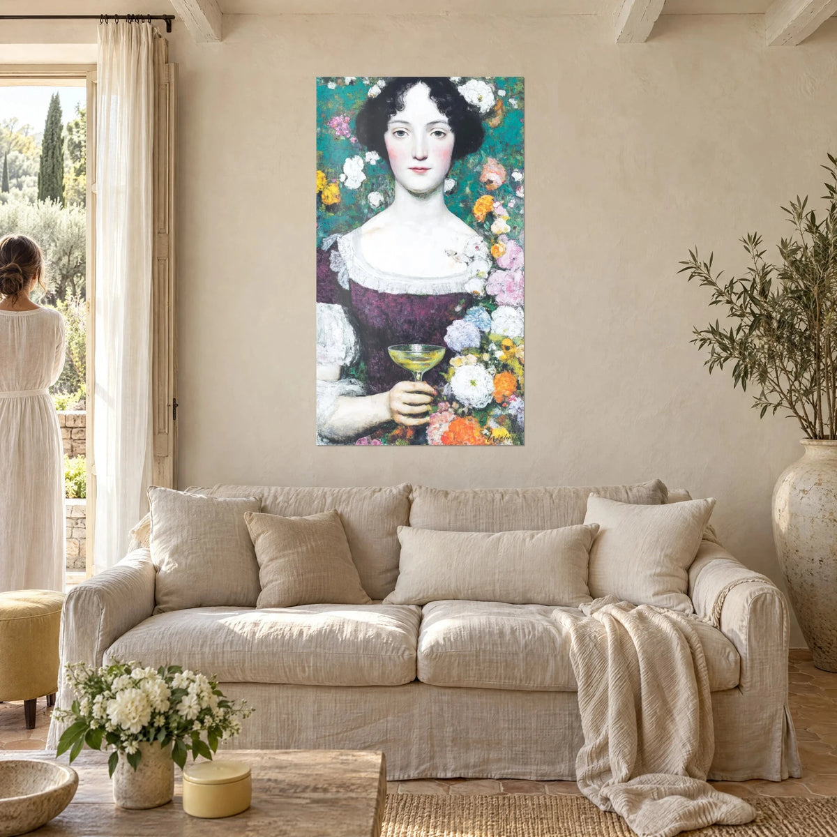 Wall art portrait of a brunette woman holding a champagne flute, plum dress and white flowers, above a sofa in a bright living room