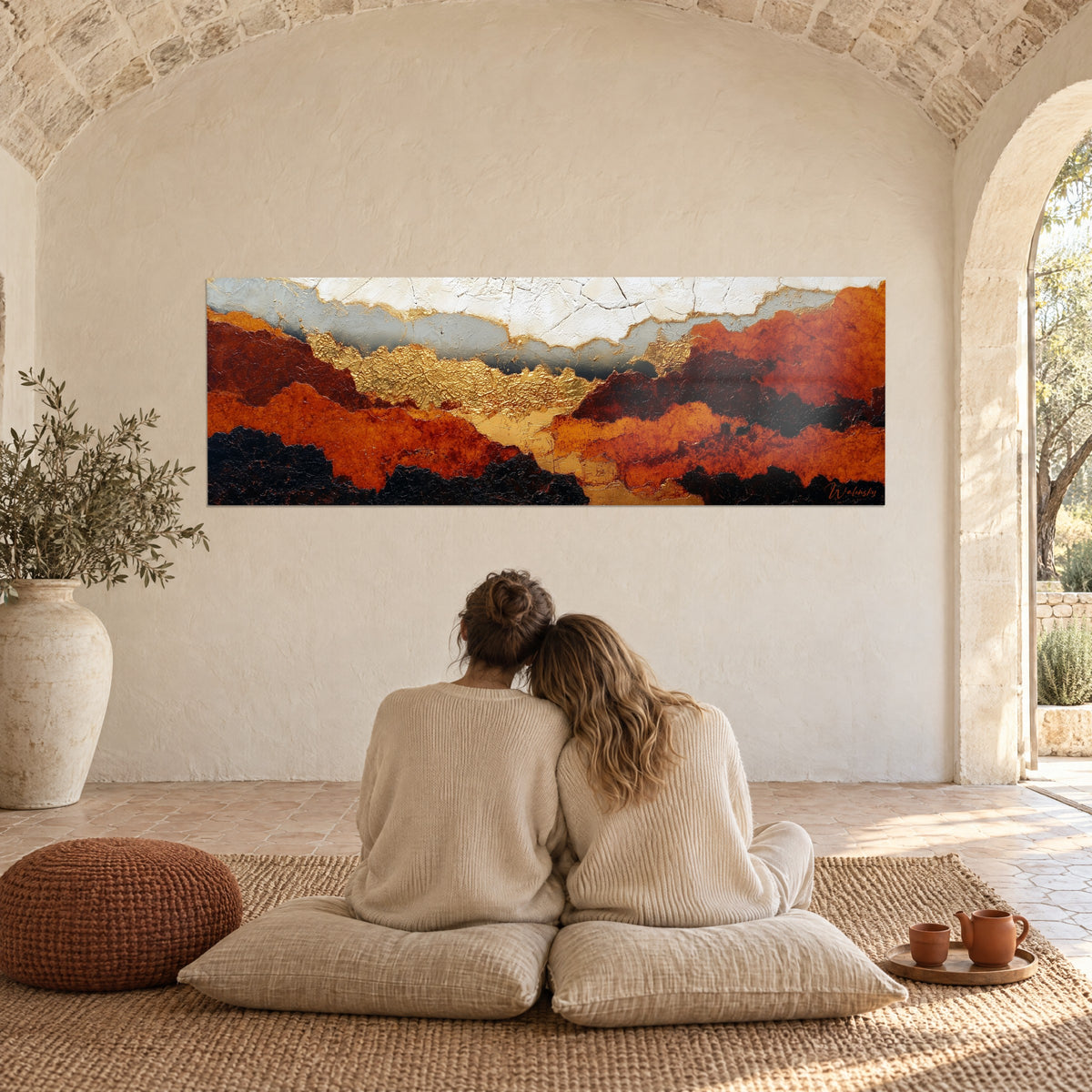 Wall art sweeping expanse of ochre and black hills with gold touches, couple embracing from behind on cushions in a Provençal farmhouse
