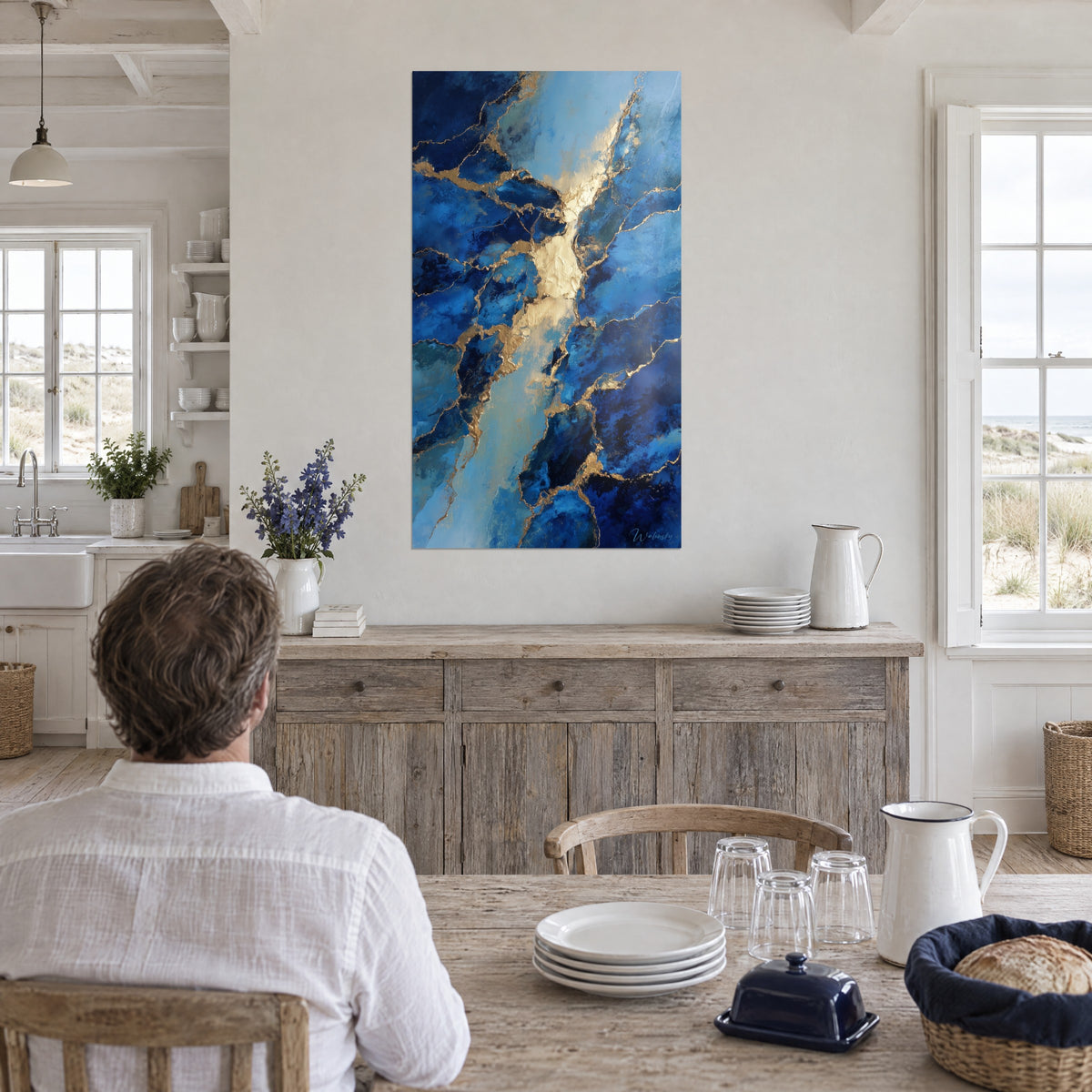 Gemälde mit goldenem Fluss inmitten von marineblauen und türkisen Splittern, Mann von hinten am Tisch in einer weißen Küche am Meer