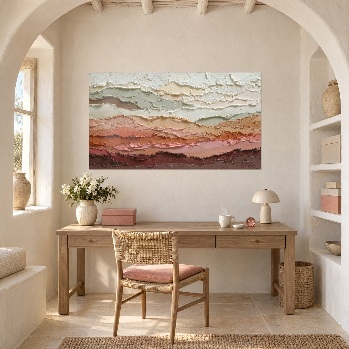 Quadro con strati d'argilla in salvia, ocra e bordeaux, appeso nell'arco di uno studio in legno chiaro con sedia in rattan