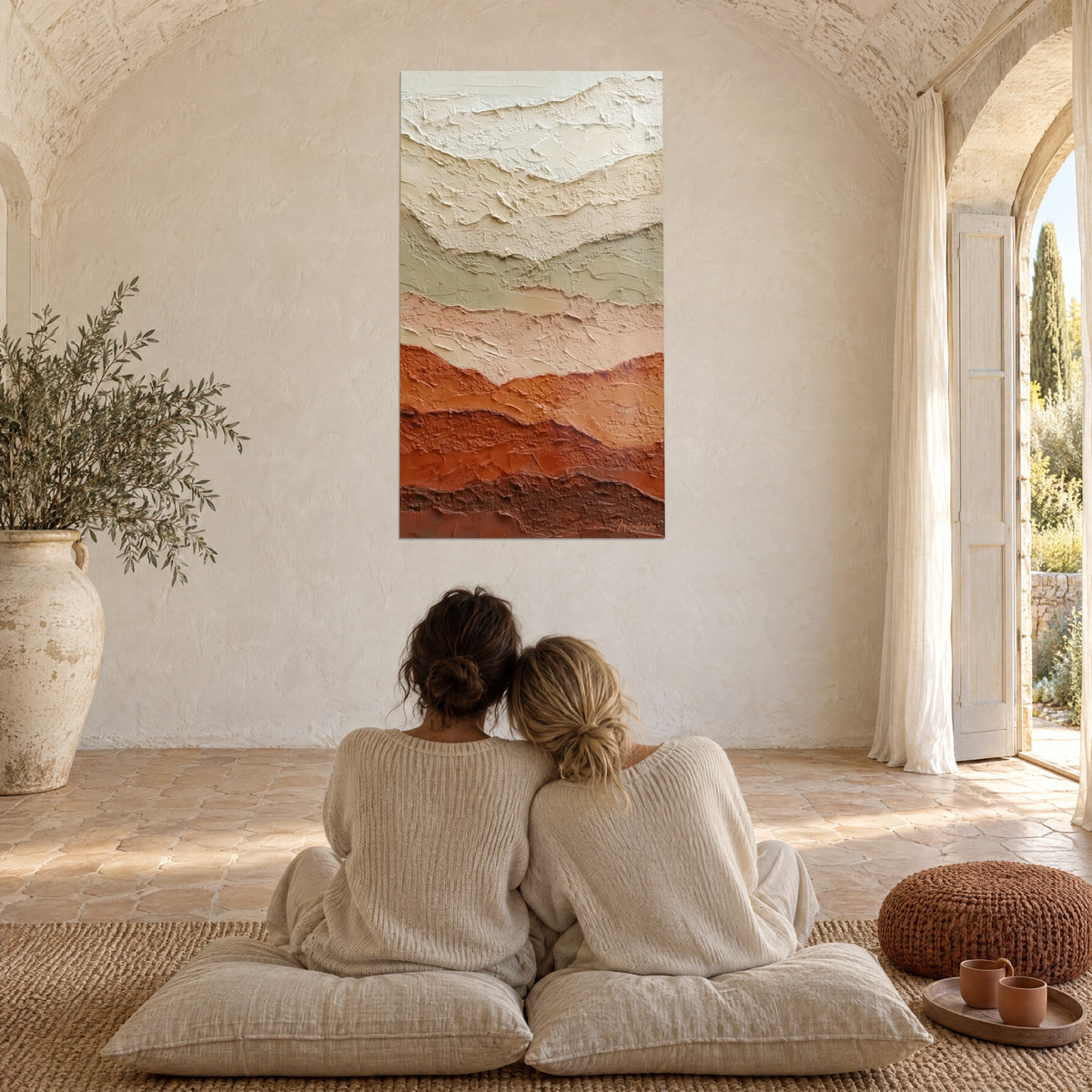 Wall art with layered mineral reliefs in ivory and deep rust, two people sit on cushions beside a whitewashed wall