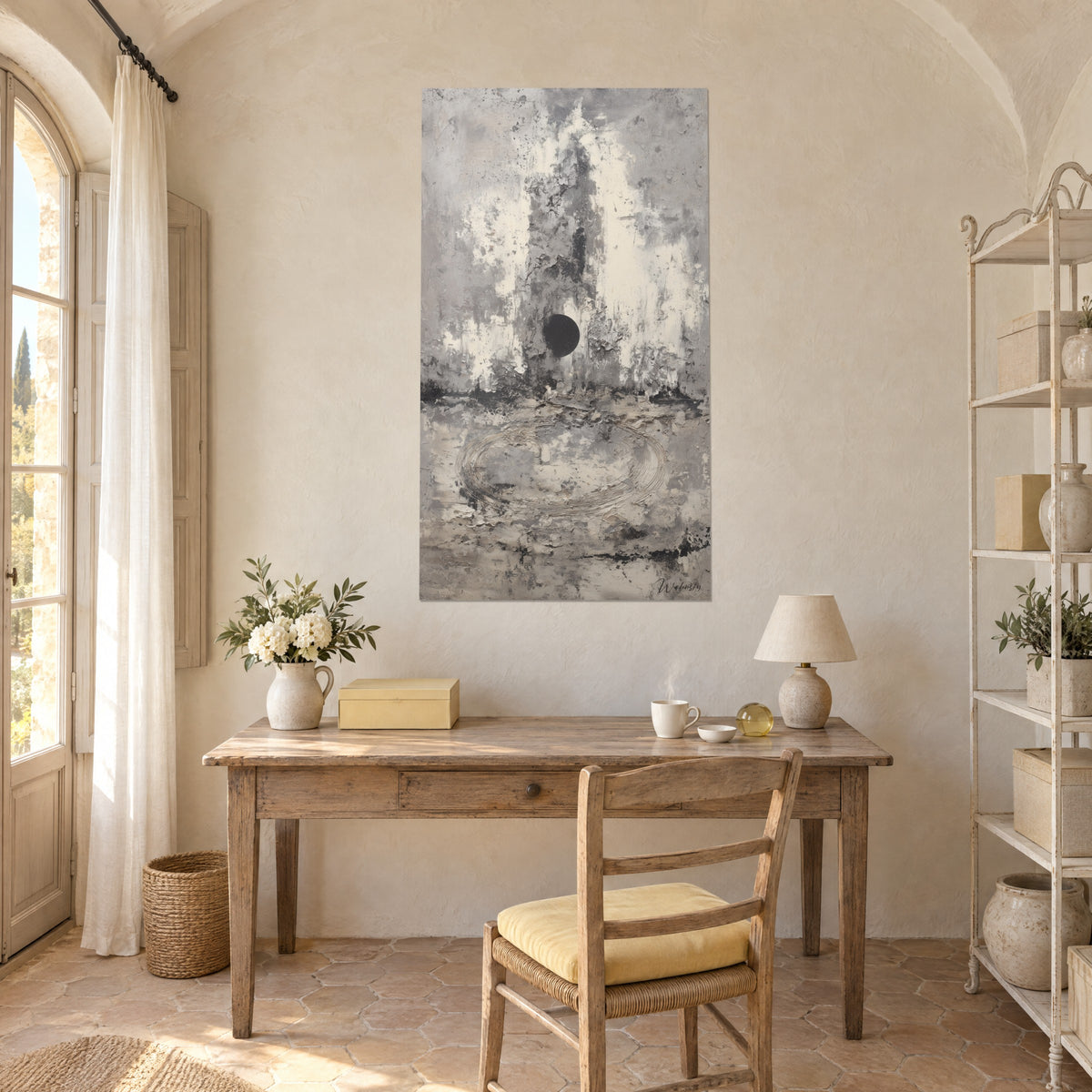 Gemälde mit verwitterter Steinwand in Graubraun und Elfenbein, Scheibe aus schwarzer Tinte in der Mitte, neben einem hellen provenzalischen Holzschreibtisch