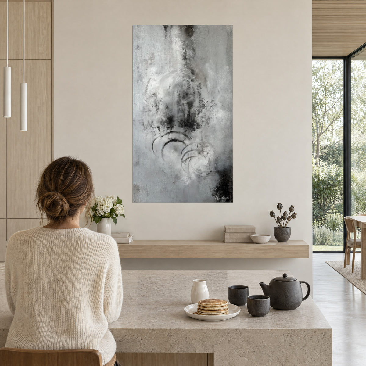 Quadro foschia grigia con schizzi di inchiostro nero, grandi cerchi sottili, di fronte a una cucina aperta in legno chiaro e pietra beige