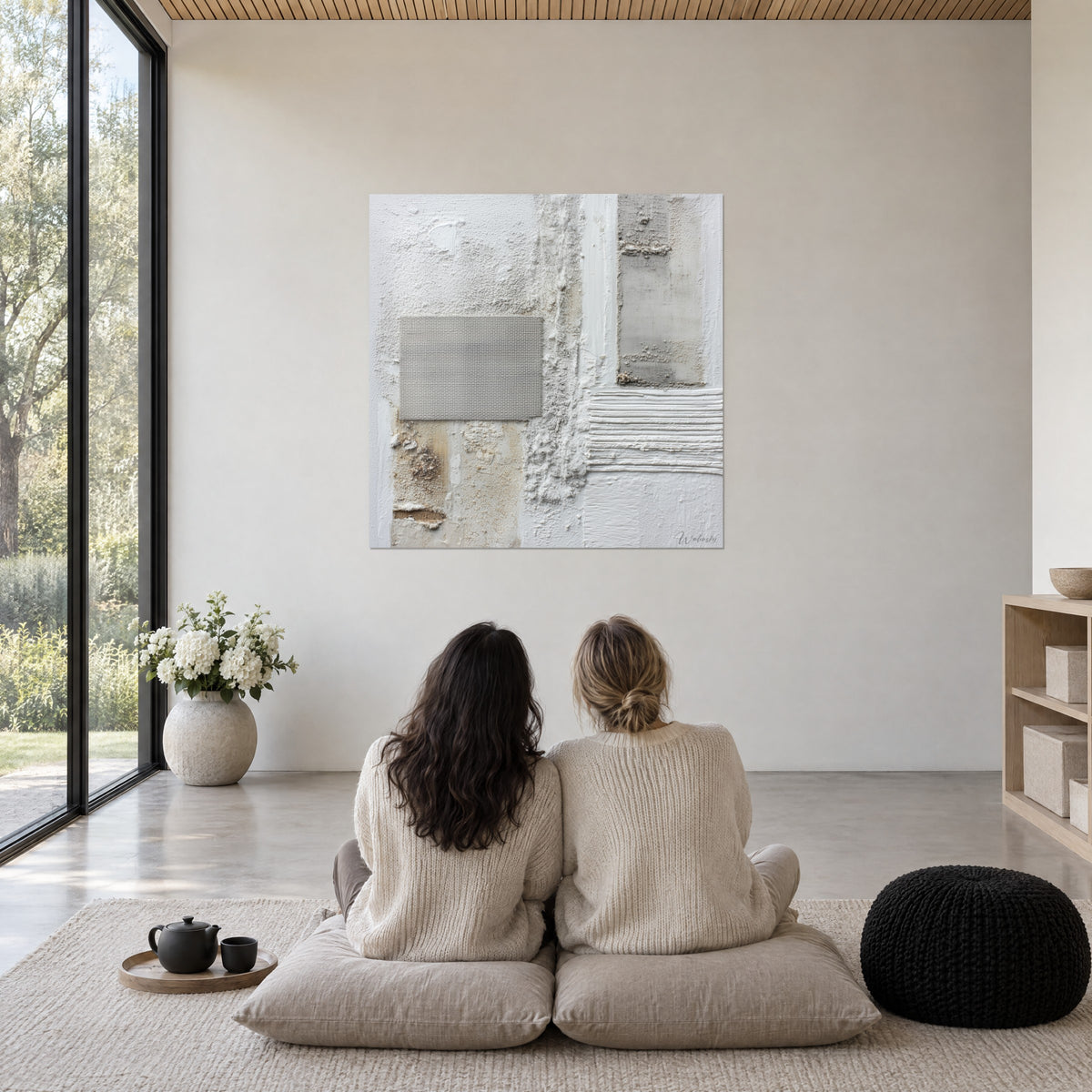 Schilderij lagen wit gips, grijs geweven stof en oker zandaccenten, twee vrouwen van achteren zittend op kussens, lichte woonkamer