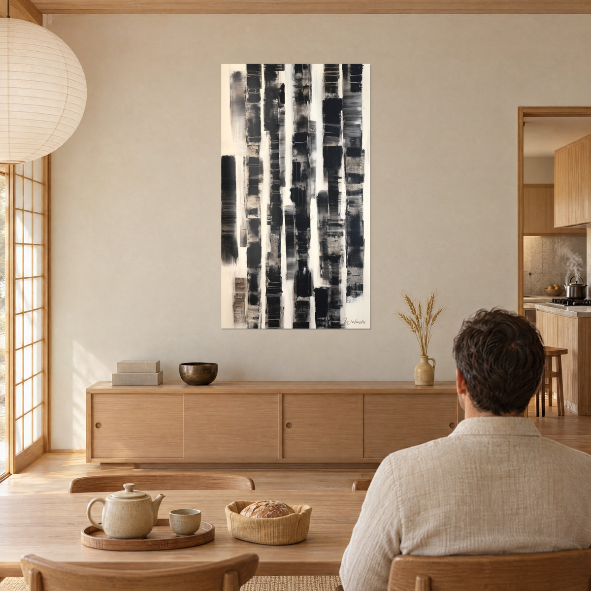 Cuadro de rayas verticales negro carbón y gris taupe sobre fondo crema, hombre de espaldas sentado a una mesa con té, salón japandi