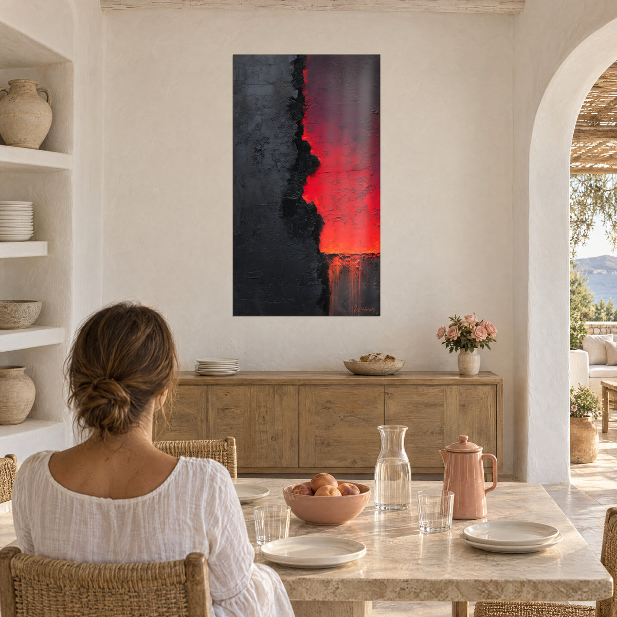 Gemälde mit rotem Feuerriss auf mattem Schwarz, Frau von hinten am Tisch sitzend, weiße Bögen und Regale, mediterranes Haus