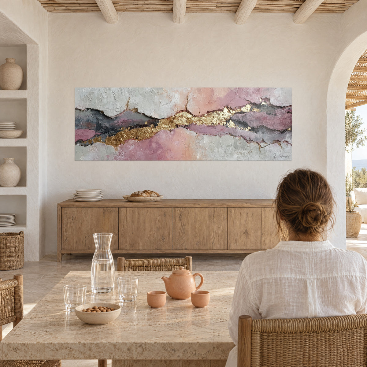 Cuadro de geoda abstracta pastel recorrida por una coulée dorada, mujer con camisa blanca en una mesa de piedra, té y frutero