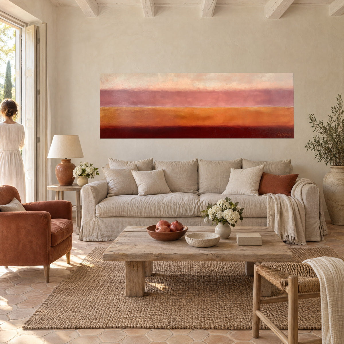 Cuadro con franjas horizontales naranja y burdeos sobre un sofá beige, una mujer de vestido blanco de espaldas, encima de un sofá en un salón luminoso