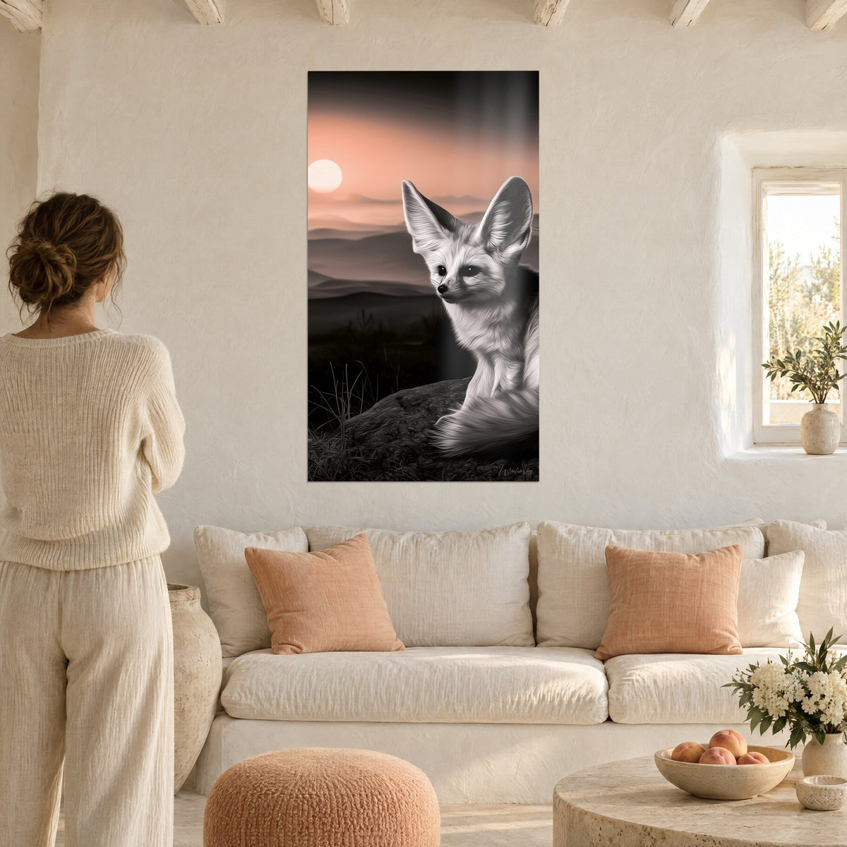 Wall art desert fox with big ears, silvery grey against salmon pink sky, seen by a woman above a sofa in a bright living room