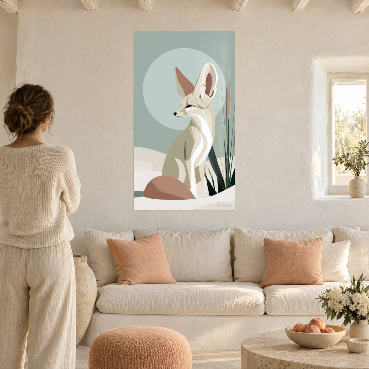 Wall art fennec fox with huge cream ears and terracotta pink in front of a blue-grey disc, woman from behind, above a sofa in a bright living room