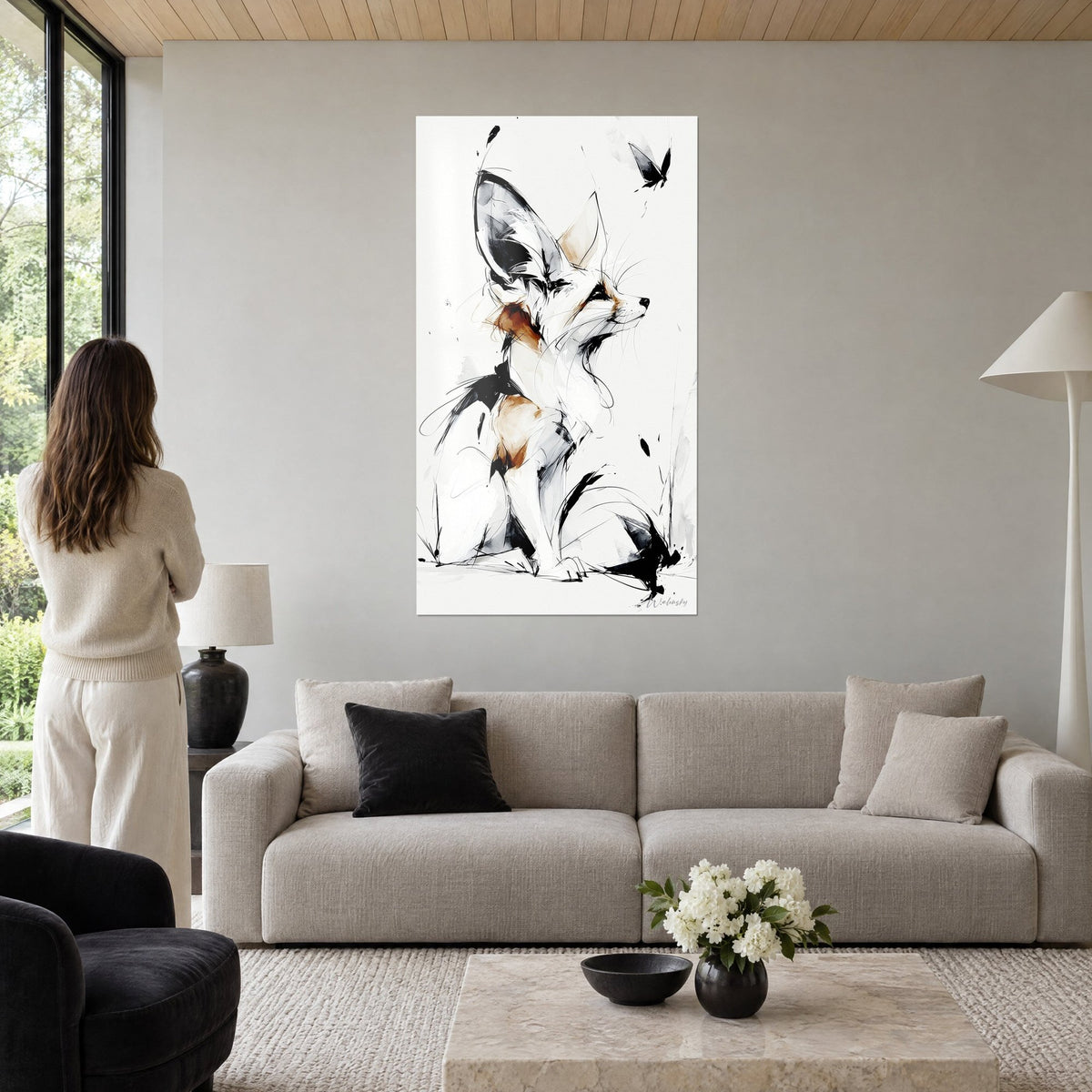 Wall art desert fox with large ears inked in black and ochre, butterfly in flight, woman seen from behind above a sofa in a bright living room