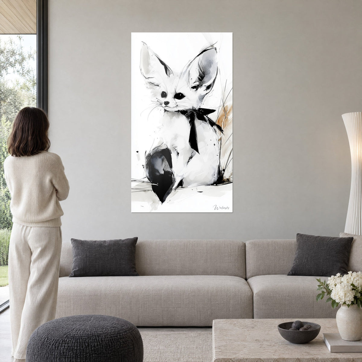 Wall art white fennec fox with large ears and black bow, grey wash and ink, woman seen from behind, above a sofa in a bright living room