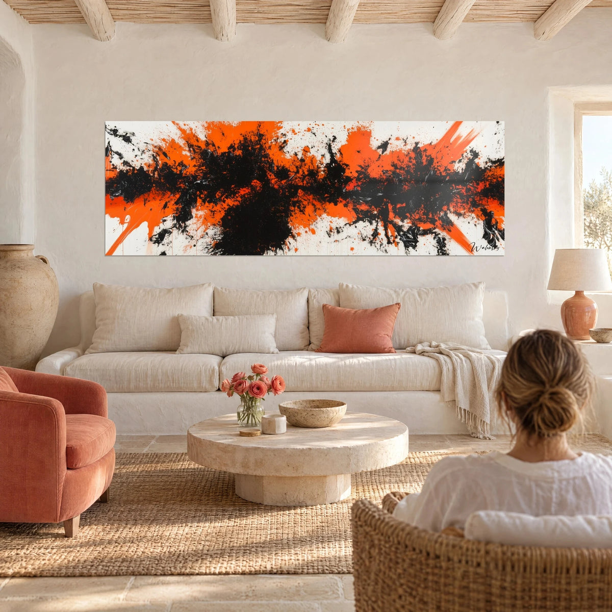 Quadro esplosione arancio e nero su fondo bianco, schizzi vividi, una donna di spalle, sopra un divano in un soggiorno luminoso