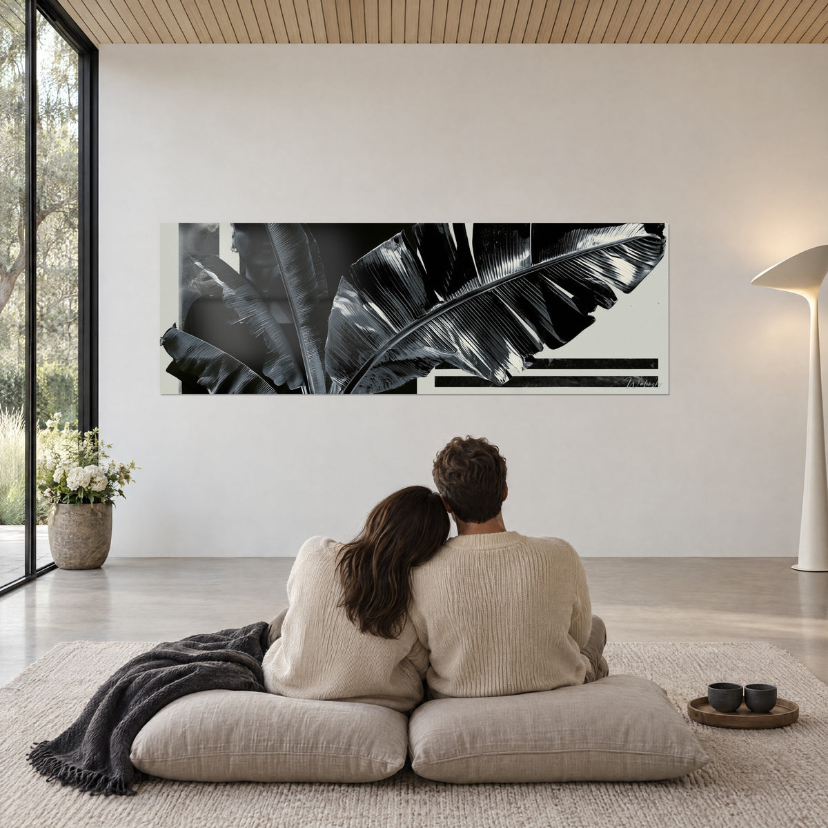 Tableau nervures de palmes brillantes noir et argent, fond ivoire, couple de dos sur coussins beiges, plaid gris, salon lumineux
