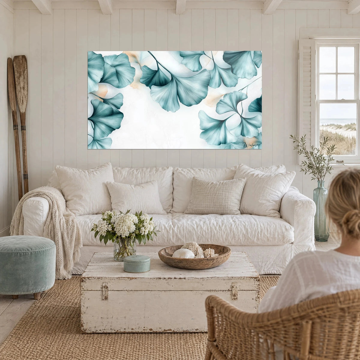 Tableau ginkgo aquarellé aux éventails turquoise et pêche sur fond marbré blanc, au-dessus d'un canapé dans un salon lumineux