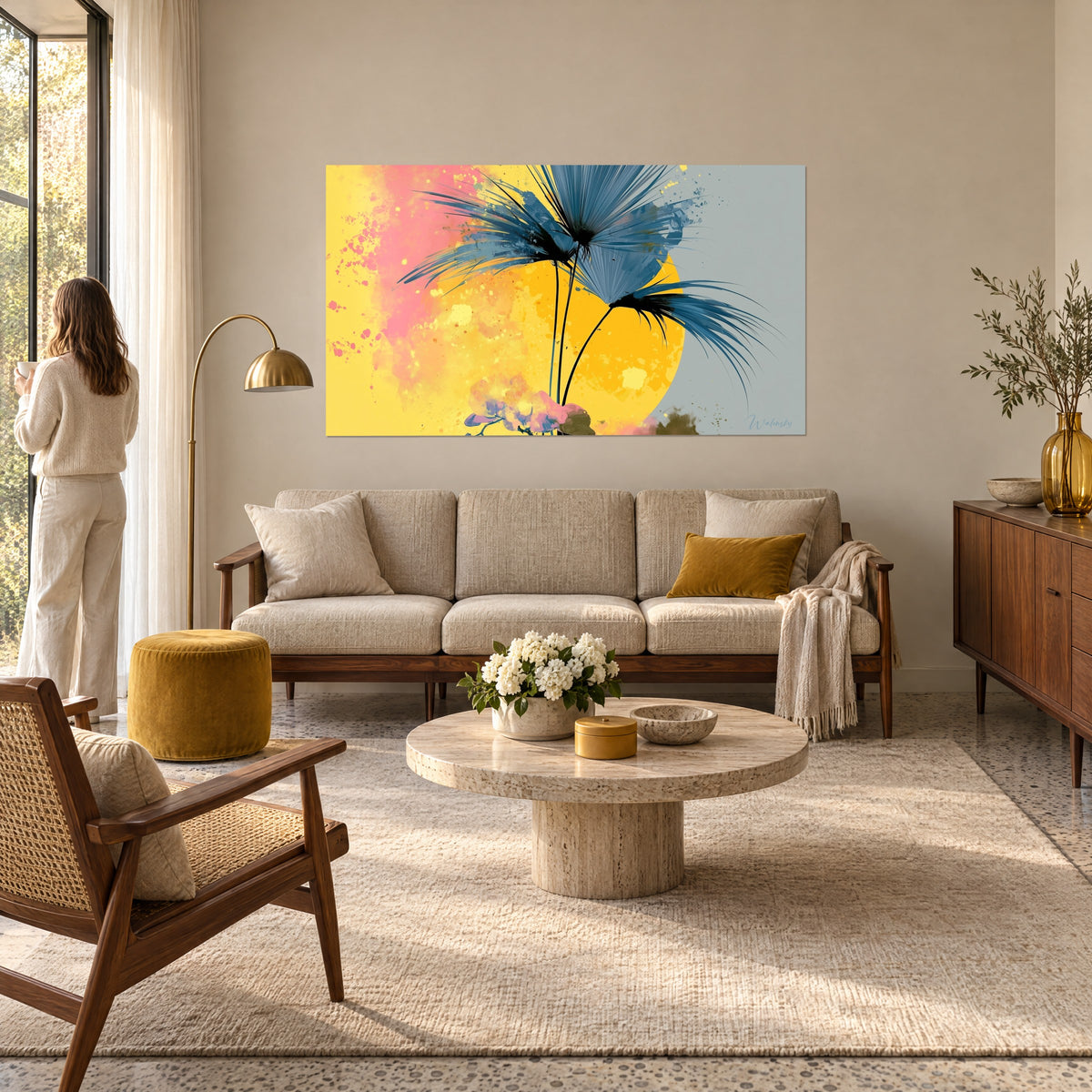 Tableau palme bleu ardoise en éventail devant un soleil jaune, éclaboussures roses, femme de dos, au-dessus d'un canapé dans un salon lumineux