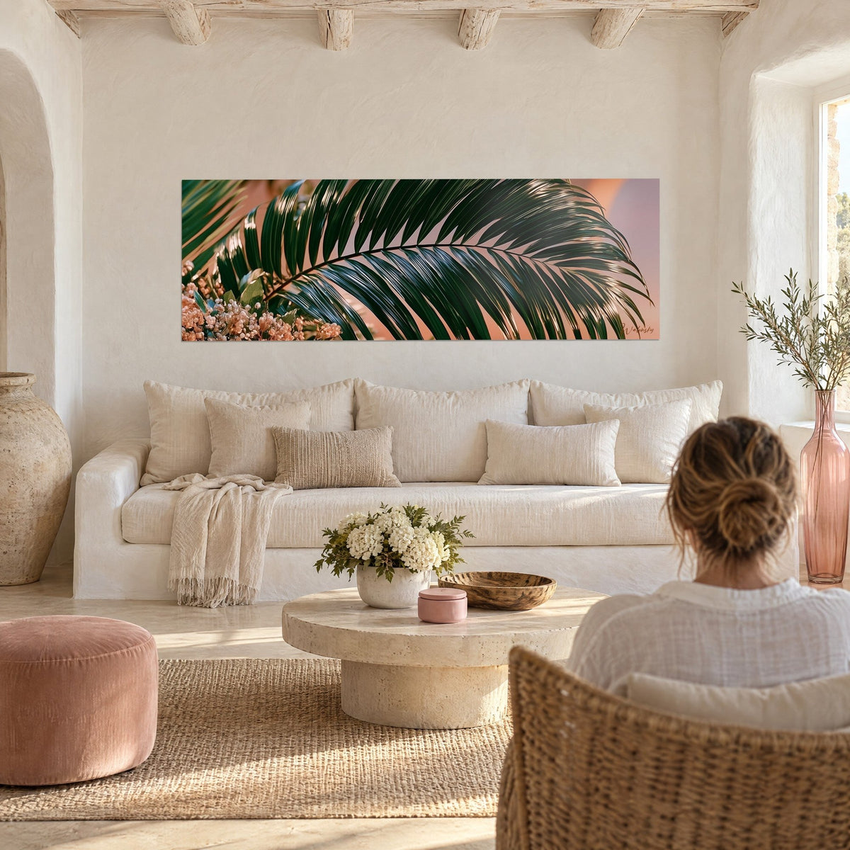 Wall art with an arched dark green palm frond on a peach background, dried flowers at the bottom, above a sofa in a bright living room