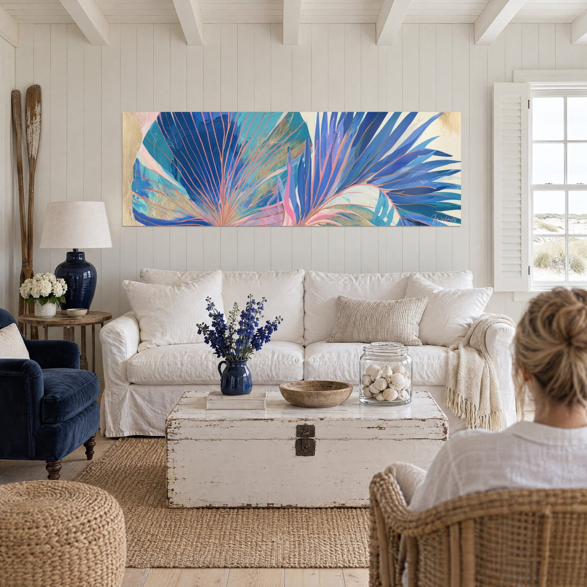 Wall art fan of indigo and turquoise palm fronds, salmon pink veins, gold accents, two people seen from behind above a sofa in a bright living room
