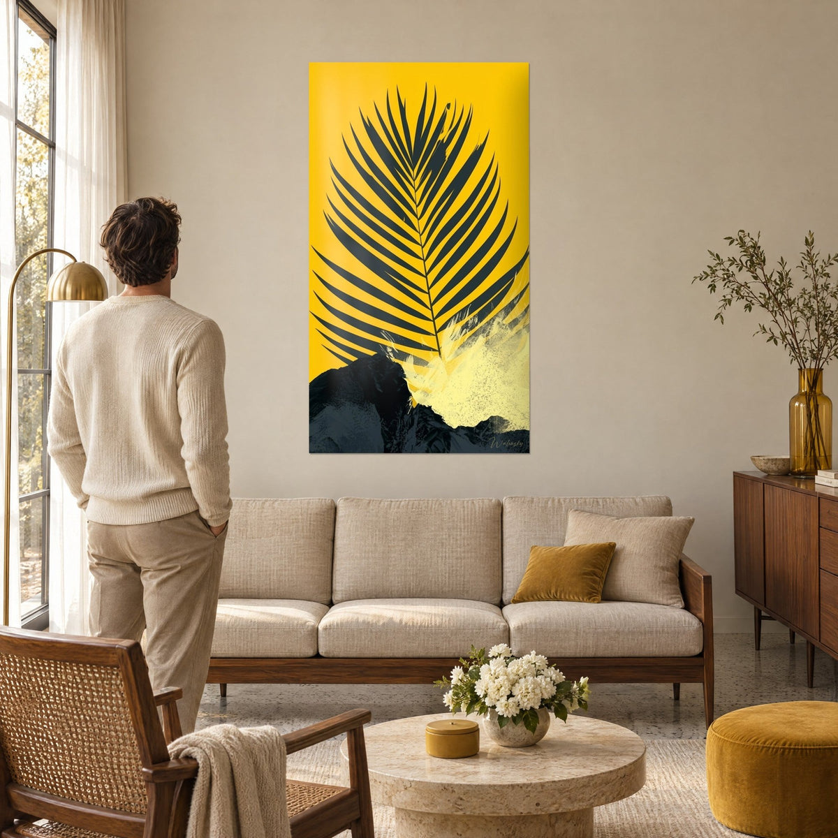 Gemälde Palmwedel anthrazit auf sonnengelbem Grund, cremefarbener Spritzer, Mann von hinten, über einem Sofa in einem hellen Wohnzimmer