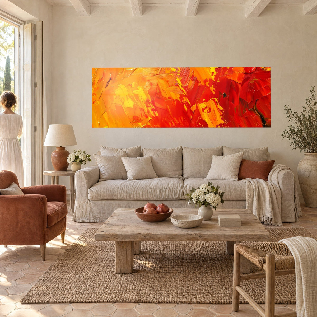 Wall art abstract flames in vivid orange and red with thick palette-knife strokes, a woman seen from behind, above a sofa in a bright living room