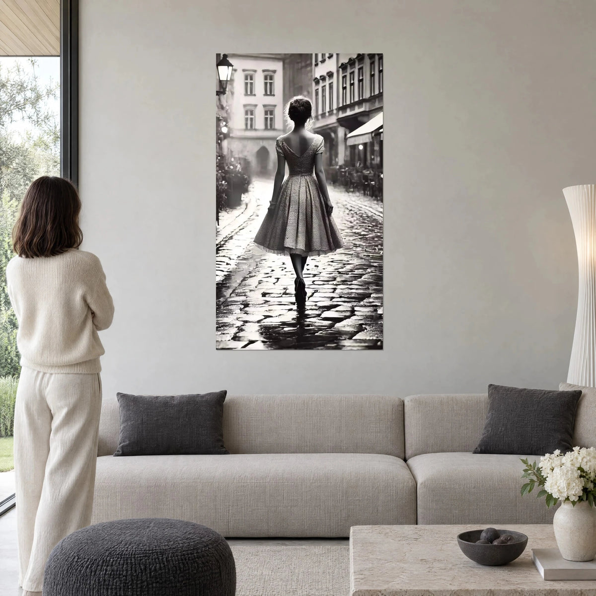 Quadro giovane donna di spalle con abito svasato su acciottolato bagnato, bianco e nero, sopra un divano in un soggiorno luminoso